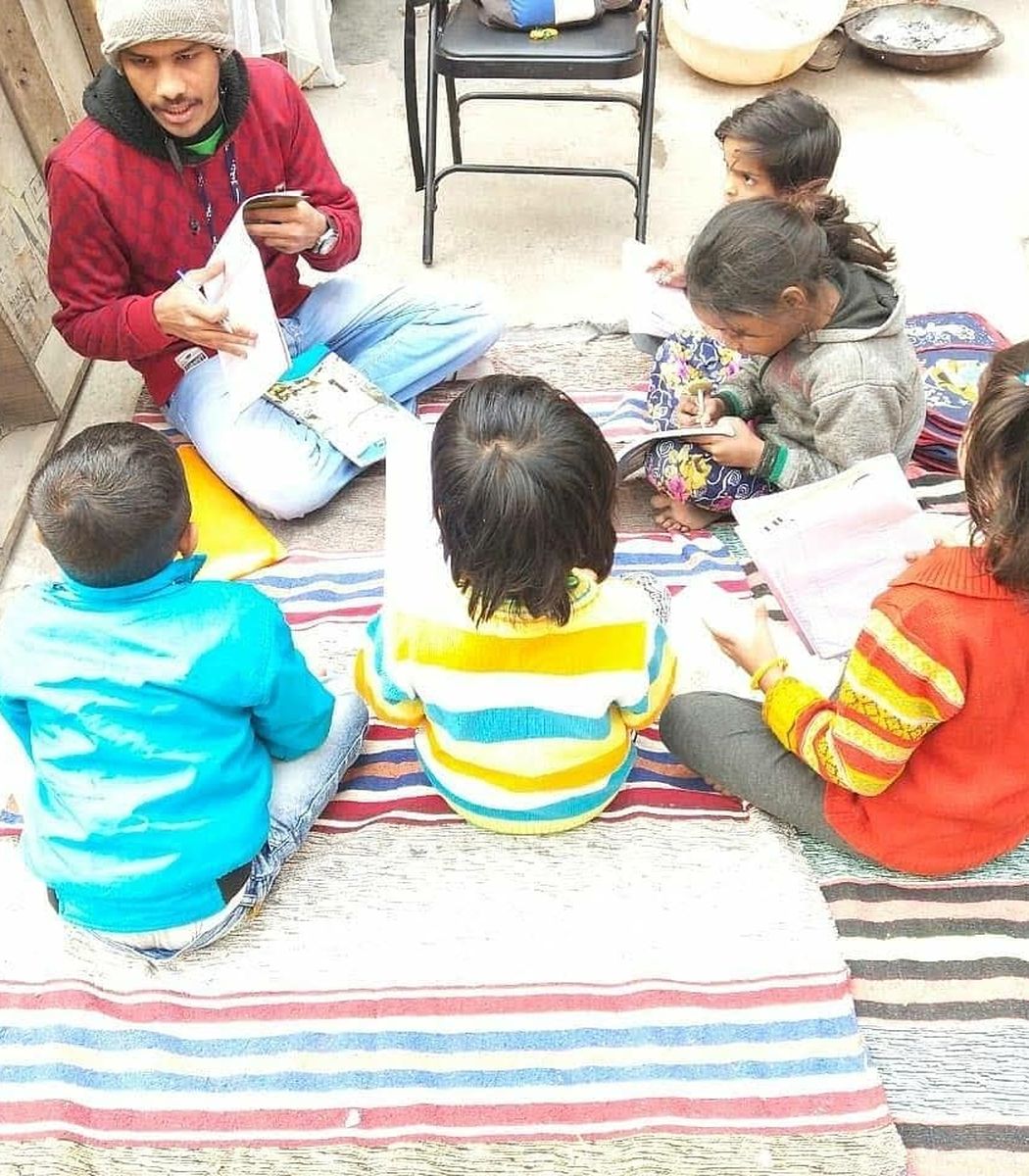 A volunteer teaching a small group of children sitting on mats